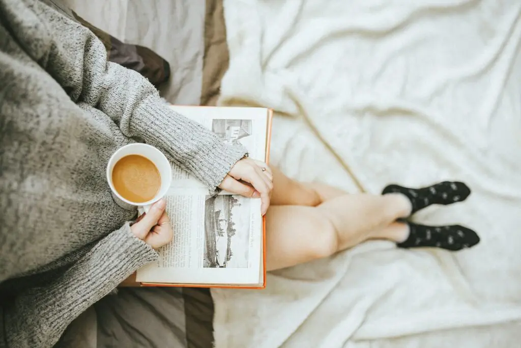 Achieve Radiant Skin: Glowing Skin at Home in 2 Days 6 woman holding a cup of coffee at right hand and reading book on her lap while holding it open with her left hand in a well-lit room