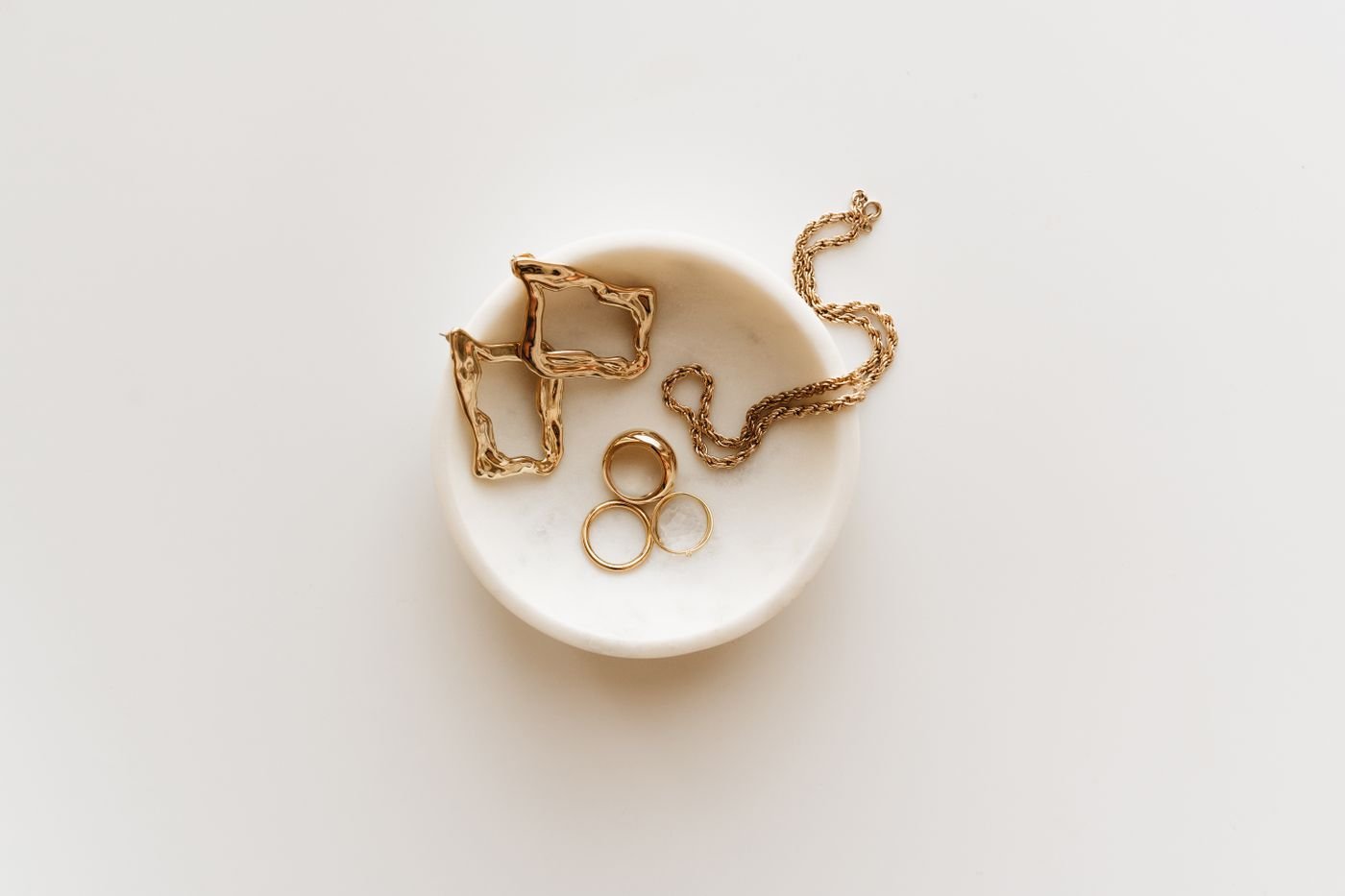 Mejuri Review: Is the Everyday Fine Jewelry Brand Worth It? 3 Illustrative arrangement of gold jewelry on a light surface